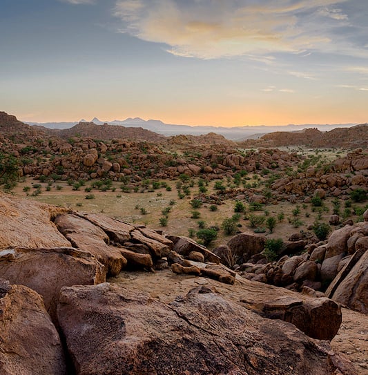 Massive granite boulders scattered across the rugged landscape of Damaraland at sunset.