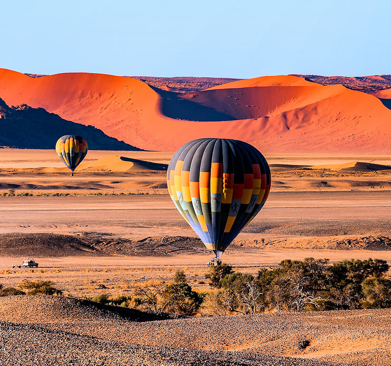Hot air balloons flying over a desert plain with red sand dunes in Sossusvlei.