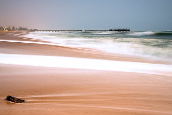 Ocean waves washing ashore on the sandy beach near the Swakopmund pier.