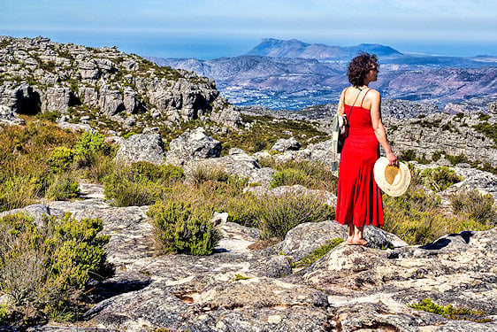 Woman in a red dress holding a sunhat and looking out over mountain views in Cape Town.