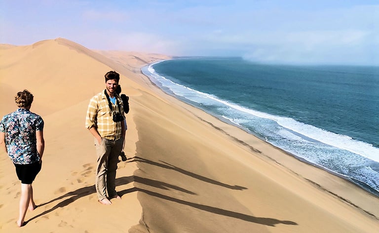 Tourists walking along the crest of a massive sand dune where it meets the ocean, Sandwich Harbour near Swakopmund, Namibia