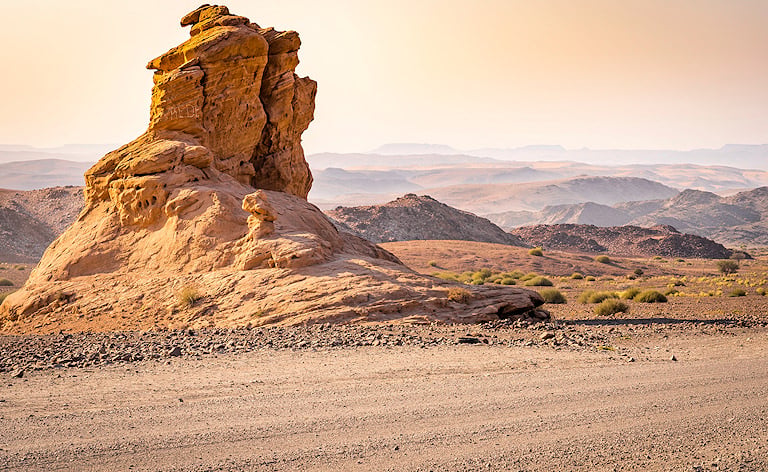Tall sandstone rock pillar standing beside a dirt road with desert hills in the background, Damaraland, Namibia.