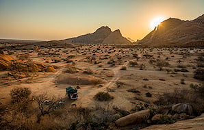 Sun setting behind granite peaks over a desert plain in Damaraland.