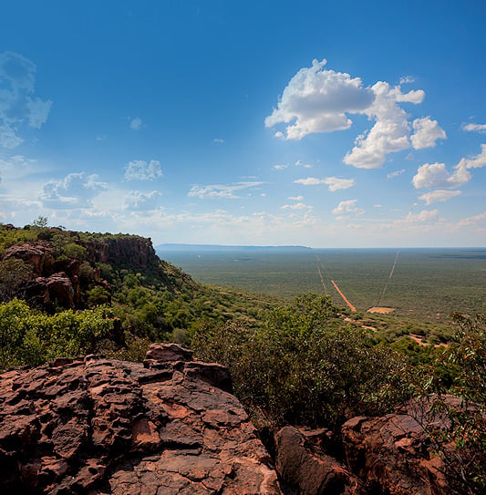 A view from the rugged red cliffs of the Waterberg Plateau looking out across a vast, flat green landscape in Namibia.