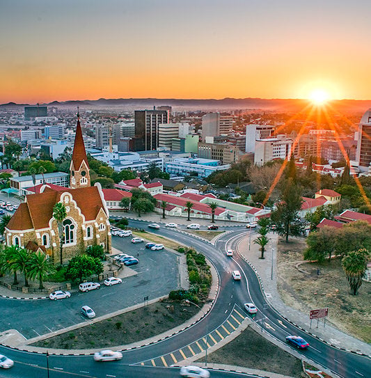 The sun setting over the Windhoek city skyline, highlighting the historic Christuskirche church on a central traffic island.