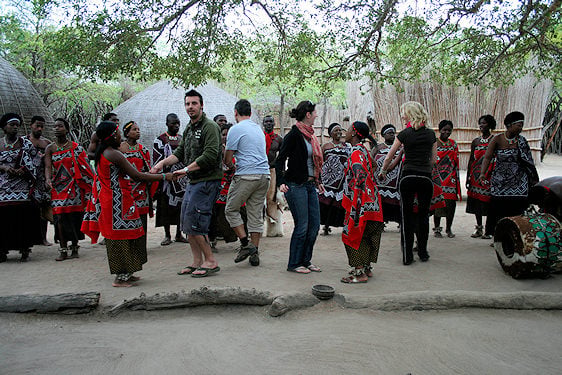 Tourists participating in a traditional dance alongside local performers at a cultural village.