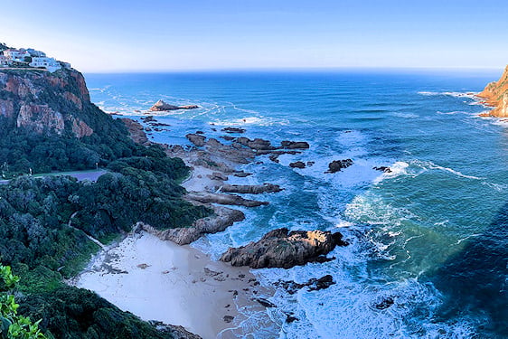 High-angle view of ocean waves breaking against a rocky cove and steep coastal cliffs.