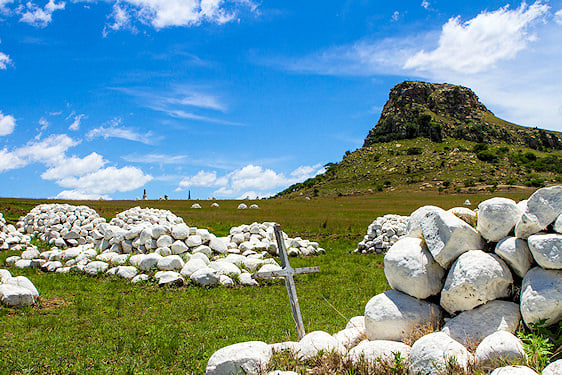 White stone grave cairns and a wooden marker on the Isandlwana battlefield.