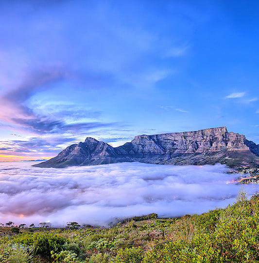 A panoramic view of Table Mountain in Cape Town, South Africa, rising above a thick blanket of low-lying clouds.