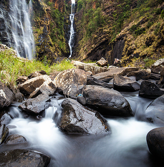 Lisbon Falls plunging down a rocky cliff with water rushing over boulders in the foreground, Mpumalanga.