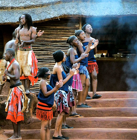 Performers singing and clapping in front of a thatched hut at Shangana Cultural Village, Mpumalanga.