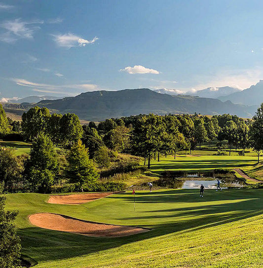 Golfers on a green with sand bunkers and a pond against a mountain backdrop in Champagne Valley.