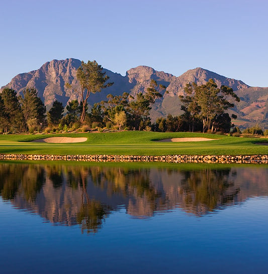 A green and sand bunkers reflected in a lake with mountains in the background in Paarl.
