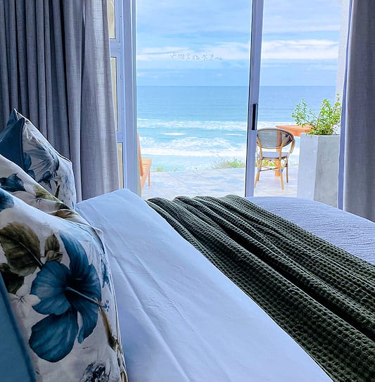 Bed looking out open sliding glass doors to a patio overlooking the ocean.