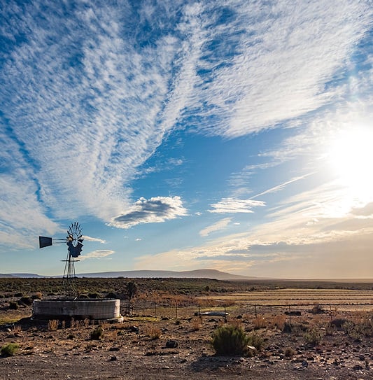 Windmill and circular water tank in the open Karoo landscape at sunset.
