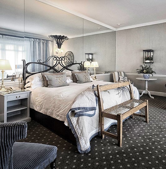 King bed guest room with a large mirrored wall, leather couch, coffee table, and wall clock in Cape Town.