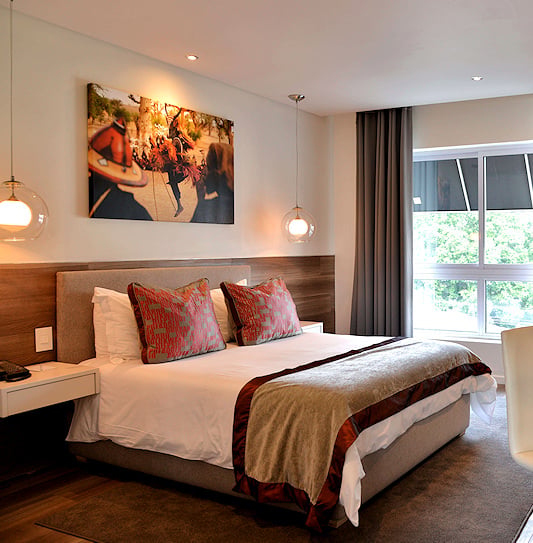 Modern guest bedroom with a king bed, desk with fresh flowers, and large window in Cape Town.