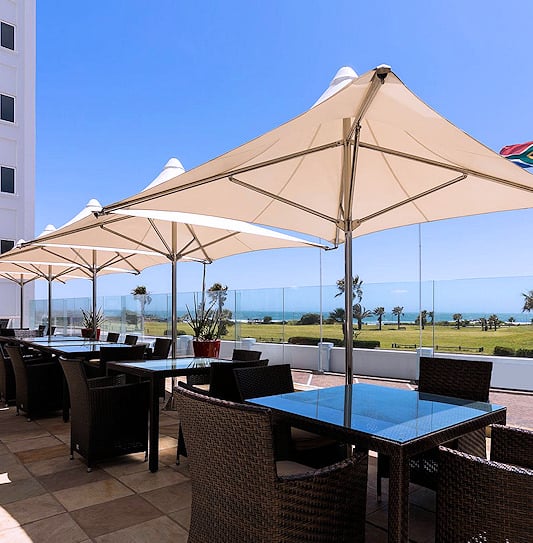 Outdoor dining patio with large sun umbrellas overlooking the Port Elizabeth coastline.