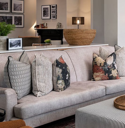 Open-plan lounge featuring a long sofa with throw pillows, an orange armchair, and a striped ottoman in Garden Route, South Africa.