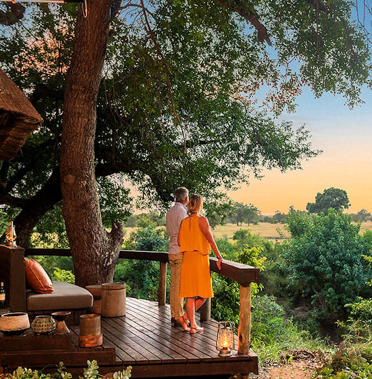 Couple on a viewing deck above the Sabi Sand bush at sunset.