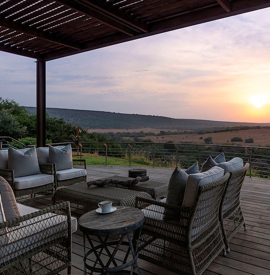 Wicker seating on a deck overlooking Eastern Cape hills in low sun.