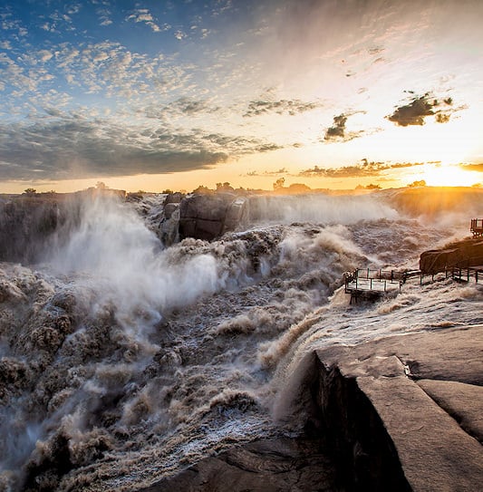 A sunset view of a powerful waterfall rushing through the rocky gorge at Augrabies Falls National Park.