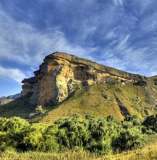The towering sandstone cliff of Brandwag Buttress rising above a green valley in Golden Gate Highlands National Park.