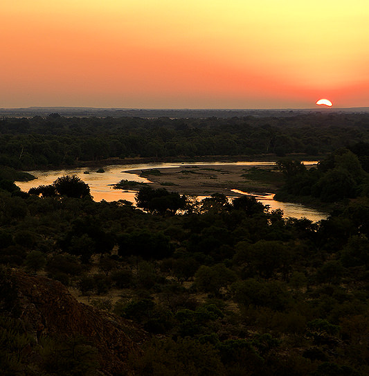 The sun on the horizon over the winding river and dense woodland of Mapungubwe National Park.