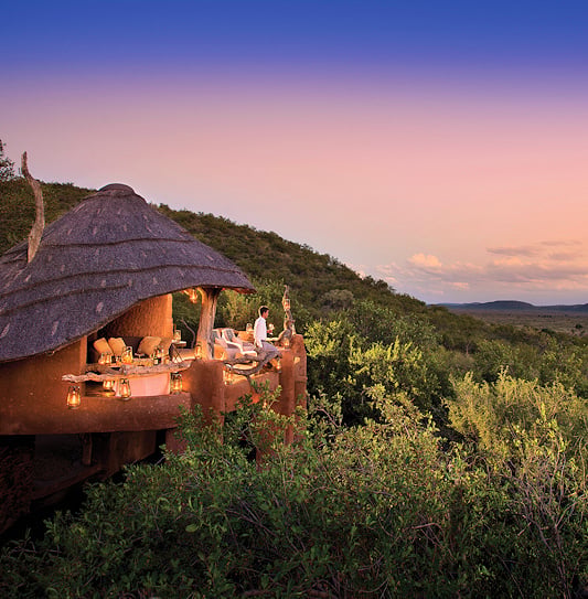 A man on a viewing deck looking out over Madikwe Game Reserve at dusk.