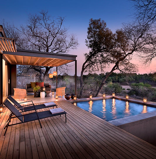 An evening scene of a private deck at the luxury Lion Sands Ivory Lodge, with a plunge pool and lanterns overlooking the Sabi Sand Private Game Reserve, South Africa.