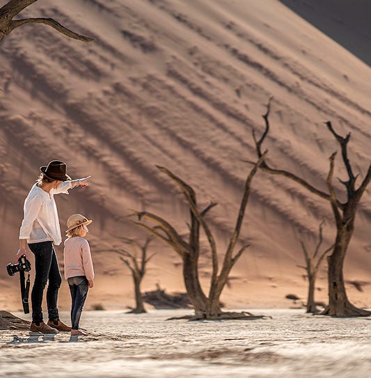 A woman and a child admiring the ancient camel thorn trees and sand dunes at Deadvlei, Sossusvlei, Namibia.