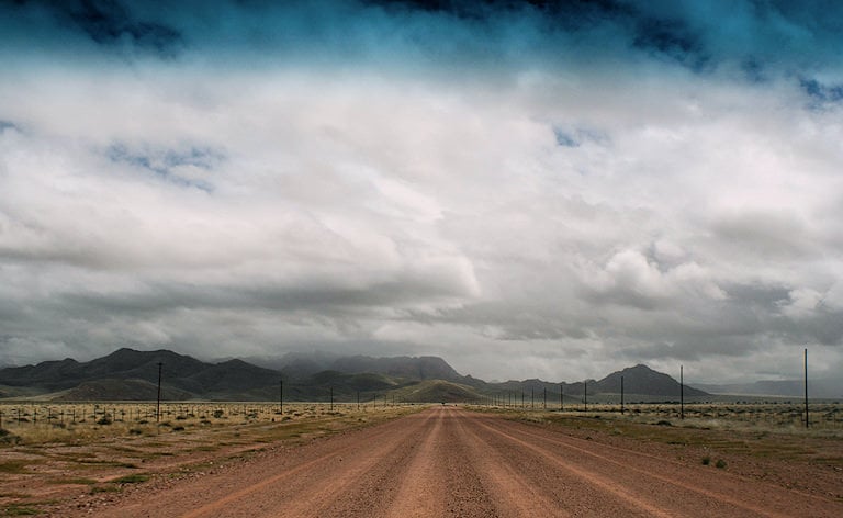 Straight dirt road heading toward mountains under an overcast sky, Sossusvlei, Namibia.