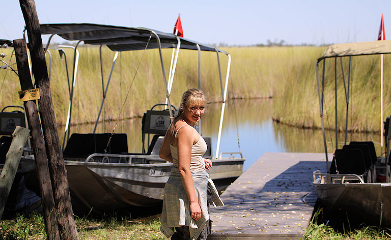 Woman walking along a wooden jetty toward motorboats moored in the water, Okavango Delta.