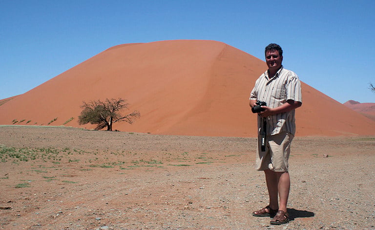Traveler with a camera standing in front of a large red sand dune, Sossusvlei, Namibia.