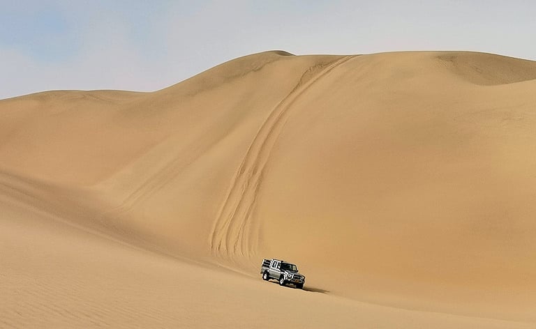 4x4 vehicle driving along the base of sand dunes at Sandwich Harbour near Swakopmund, Namibia.