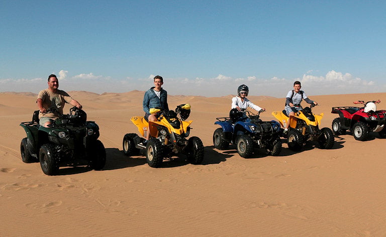 Tourists sitting on quad bikes lined up in the sand dunes, Swakopmund, Namibia.