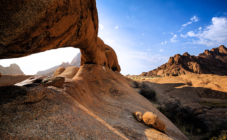 Natural granite rock arch with desert mountains under a blue sky, Spitzkoppe, Namibia.