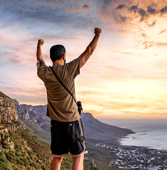 A hiker raising his hands and looking at the sunset from the top of Table Mountain, Cape Town.