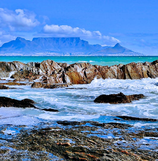 Table Mountain viewed from across the ocean with waves and rocks in the foreground, Cape Town.