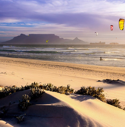 Windsurfers on the ocean at sunset under a purple sky with Table Mountain in the background, Cape Town.