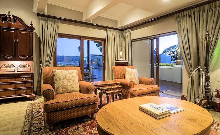 Lounge with patterned armchairs, a round wooden coffee table and sliding doors opening onto a deck.