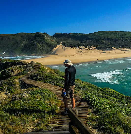 Male hiker walking on a clifftop overlooking the ocean at Robberg Nature Reserve, Plettenberg Bay.