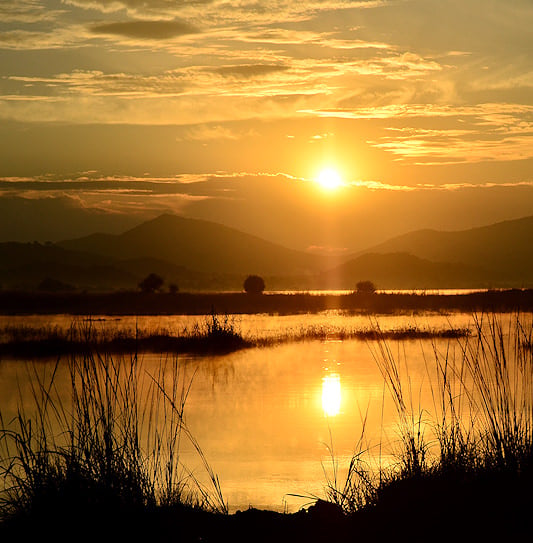 Sunrise over the mountains with a golden reflection on the river in Pilanesberg National Park, South Africa.