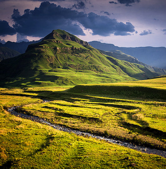 Drakensberg Mountains under sunlight breaking through dark rain clouds in KwaZulu-Natal.