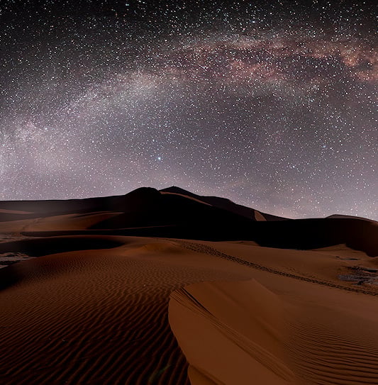Giant orange sand dunes in Sossusvlei, Namibia, under a clear starry night sky.