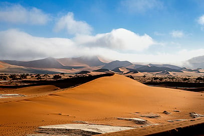 Low fog rolling over red sand dunes and desert mountains in Sossusvlei, Namibia.