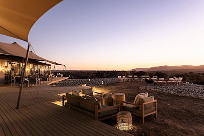 Outdoor deck and lounge seating at a luxury desert safari lodge at dusk.