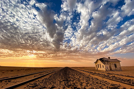 Railway tracks passing an abandoned building in the Namib Desert near Lüderitz at sunset.