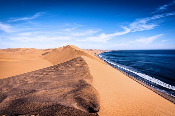 High desert sand dunes running directly into the ocean waves at Sandwich Harbour.