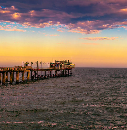 The long wooden jetty extending into the ocean at Swakopmund under a purple and orange sunset sky.